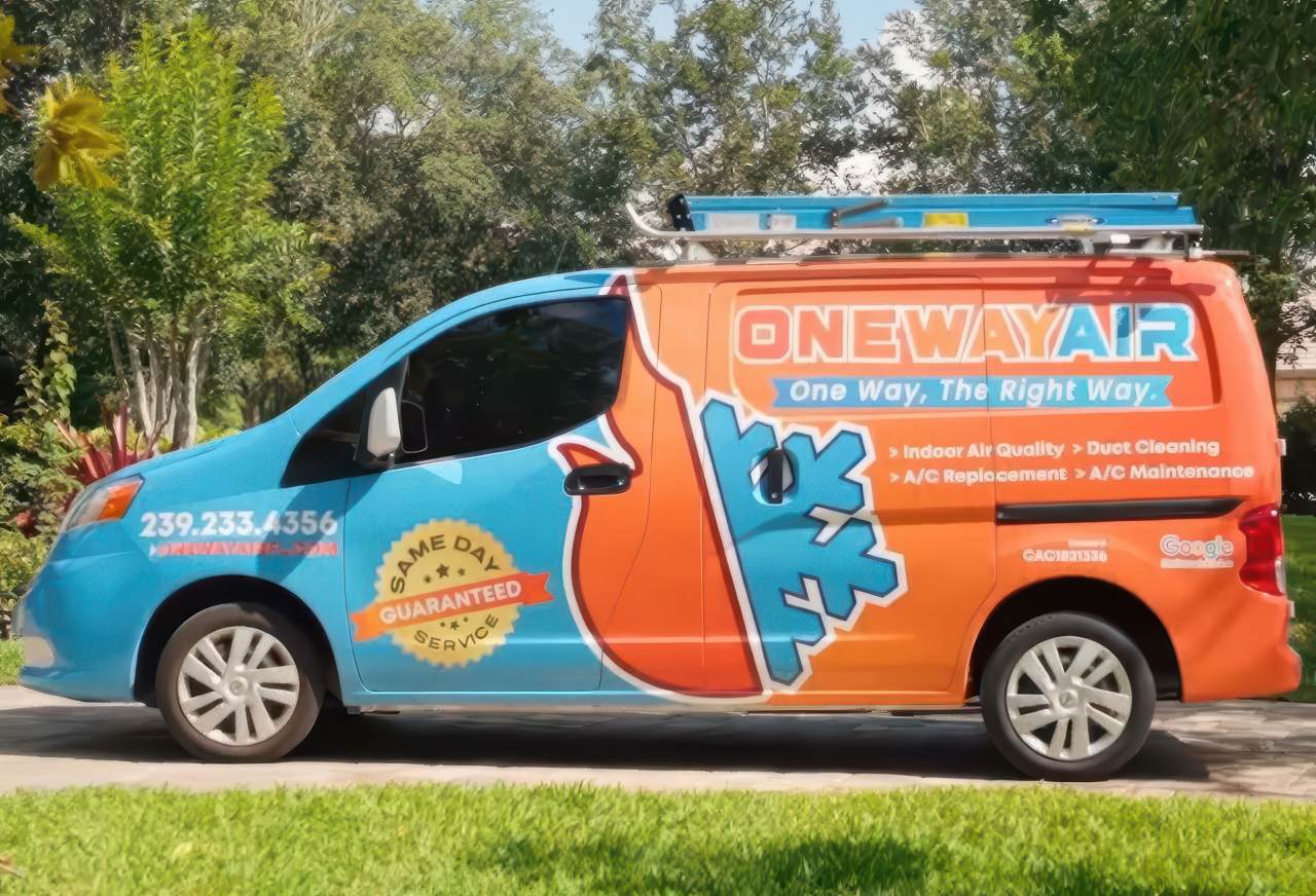 A brightly colored blue and orange One Way Air service van equipped with roof ladders is parked on a driveway in a sunny yard.