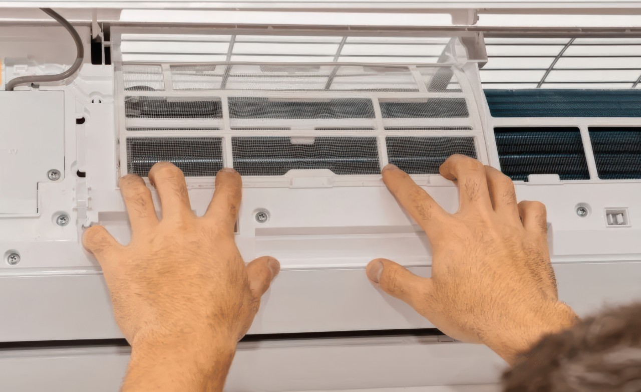 Hands pulling front panel away from indoor air conditioner to access filter and internal cooling components.