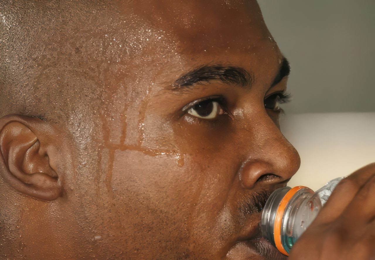 Sweating man hydrating from water bottle indoors