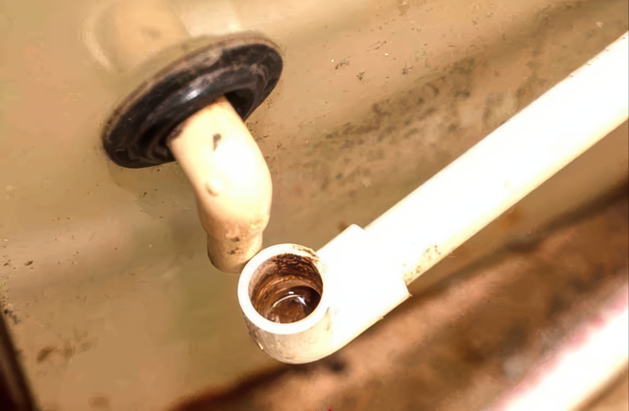 Close-up of beige pipe with black rubber seal connecting to white PVC pipe showing brown rust and mineral buildup inside