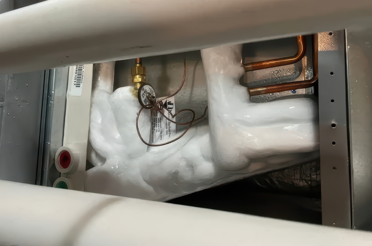 Interior view of air conditioning unit showing heavy ice accumulation covering coils, copper tubing, and metal housing components.