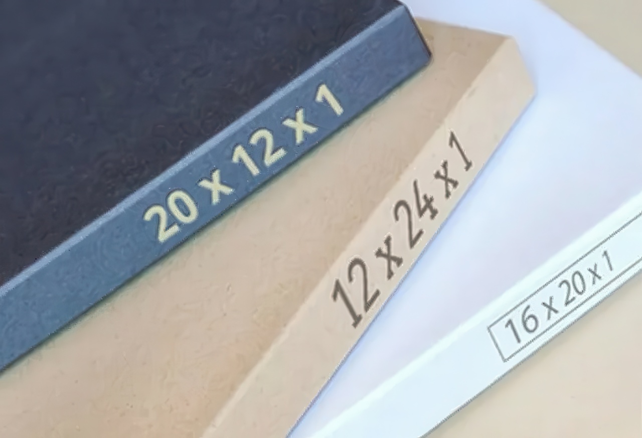 This photograph shows a stack of three air filter frames in blue, tan, and white colors. Each frame has different dimensions printed on the side, such as twelve by twenty-four by one and sixteen by twenty by one.