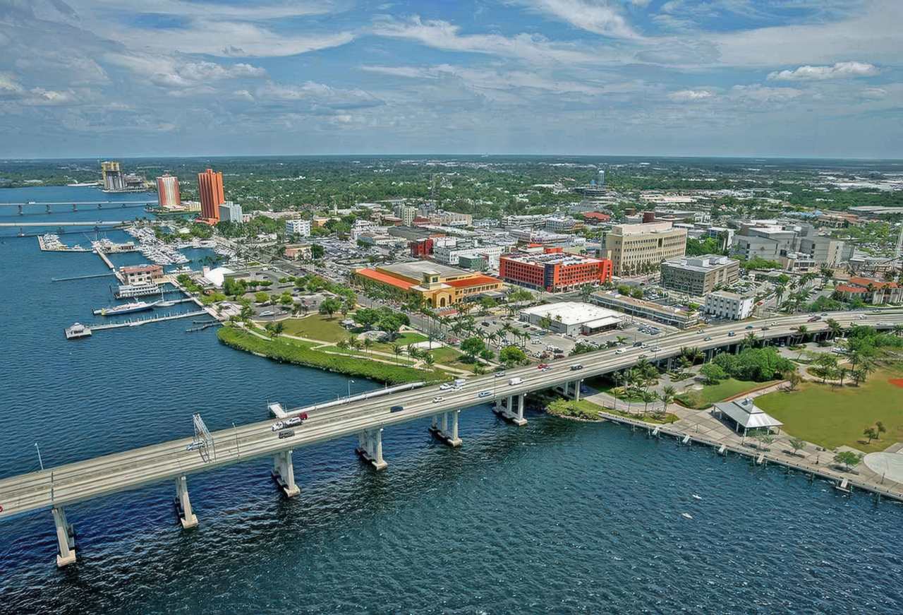 Aerial photograph of Florida coastal city showing highway bridge crossing blue water with commercial buildings, green parks, and boats docked along shoreline