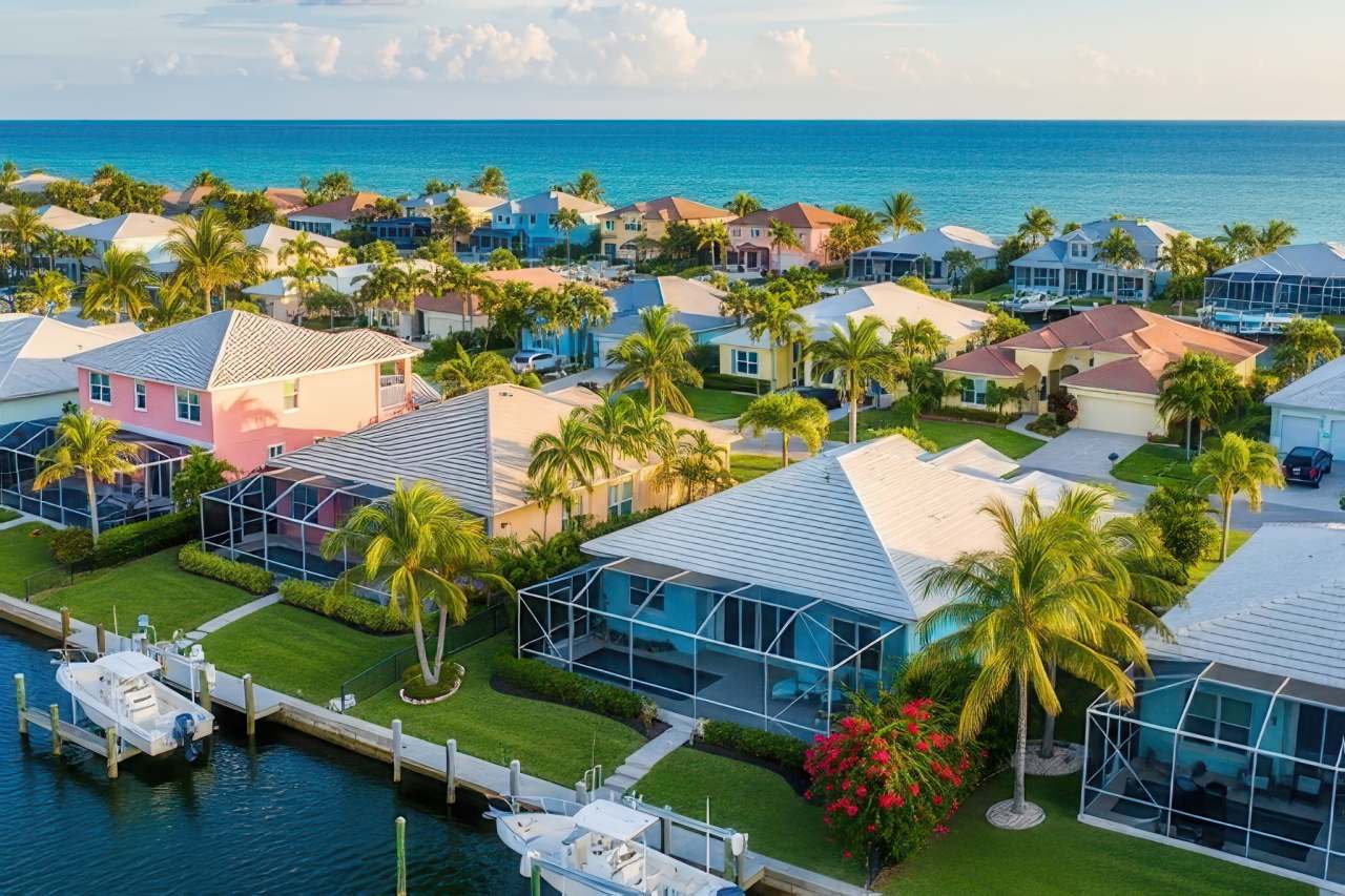 Aerial view of a coastal Florida neighborhood with colorful houses, palm trees, and boat docks along a canal near the ocean.