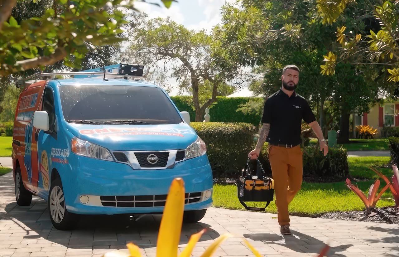HVAC technician walking toward a home with a tool bag, next to a branded ONEWAY AIR service van parked on a sunny residential driveway.