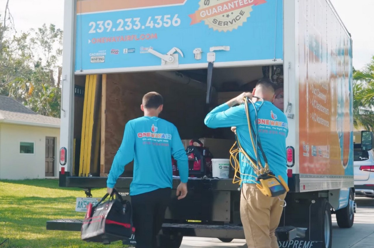 “HVAC technicians unloading tools from a branded service truck in a residential neighborhood before starting an air conditioning job.