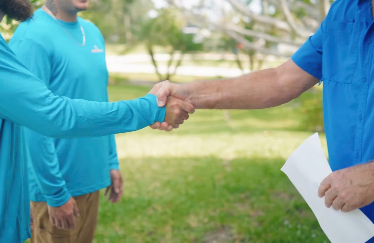 A professional handshake between a One Way Air technician and a client on a residential lawn.